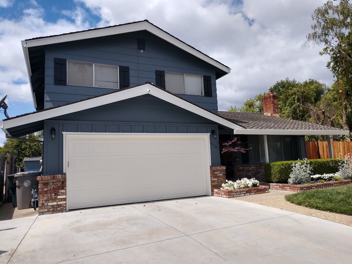 Two-story blue house with white garage door and red brick accents, blue sky in background.