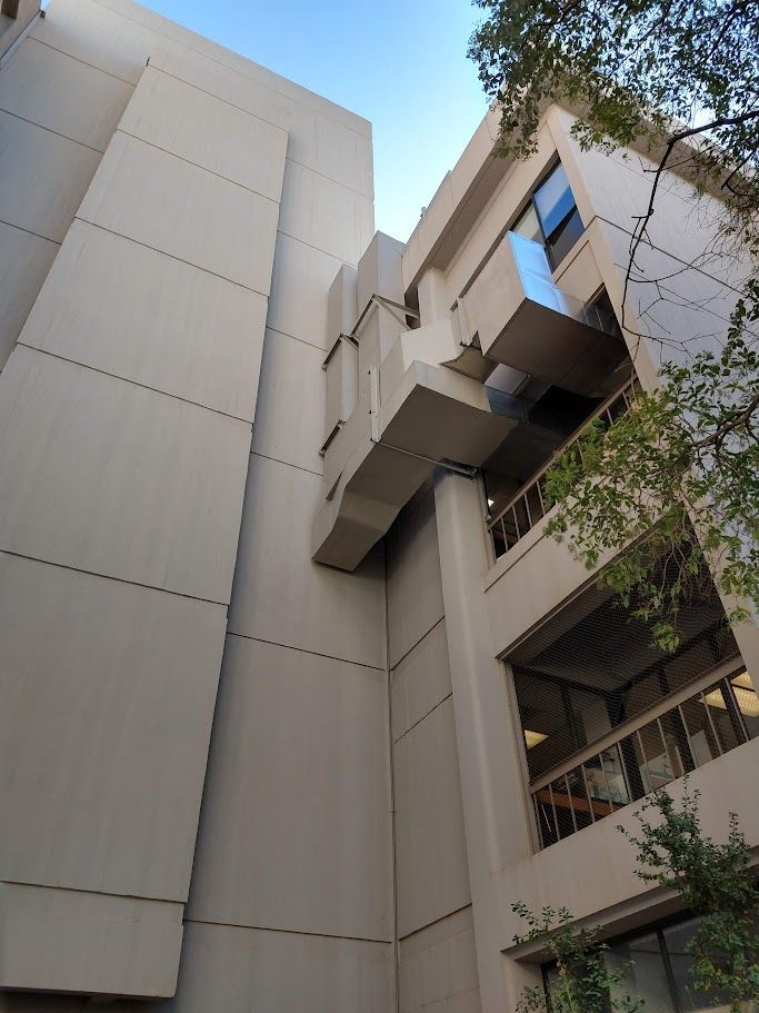 Exterior of two connected buildings with concrete walls and balconies; blue sky in background.