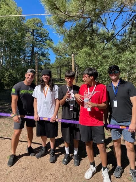 A group of young men are standing next to each other holding a purple pole.