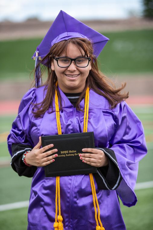 A woman in a purple graduation cap and gown is holding a diploma.