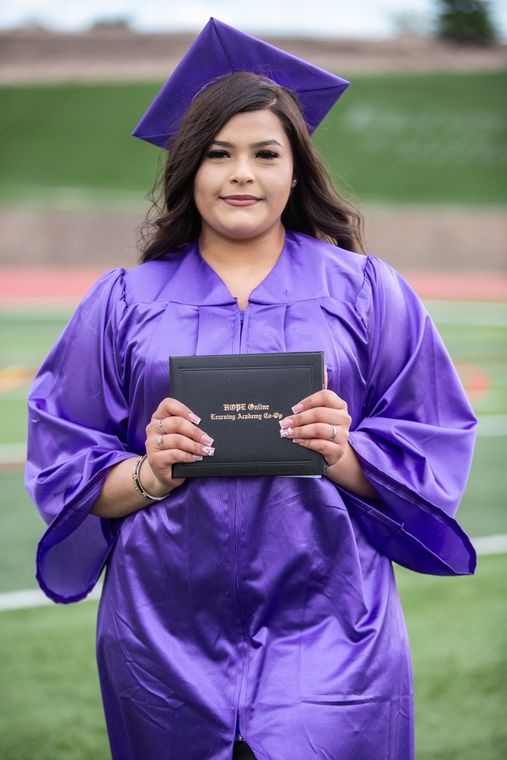 A woman in a purple graduation cap and gown is holding a diploma.