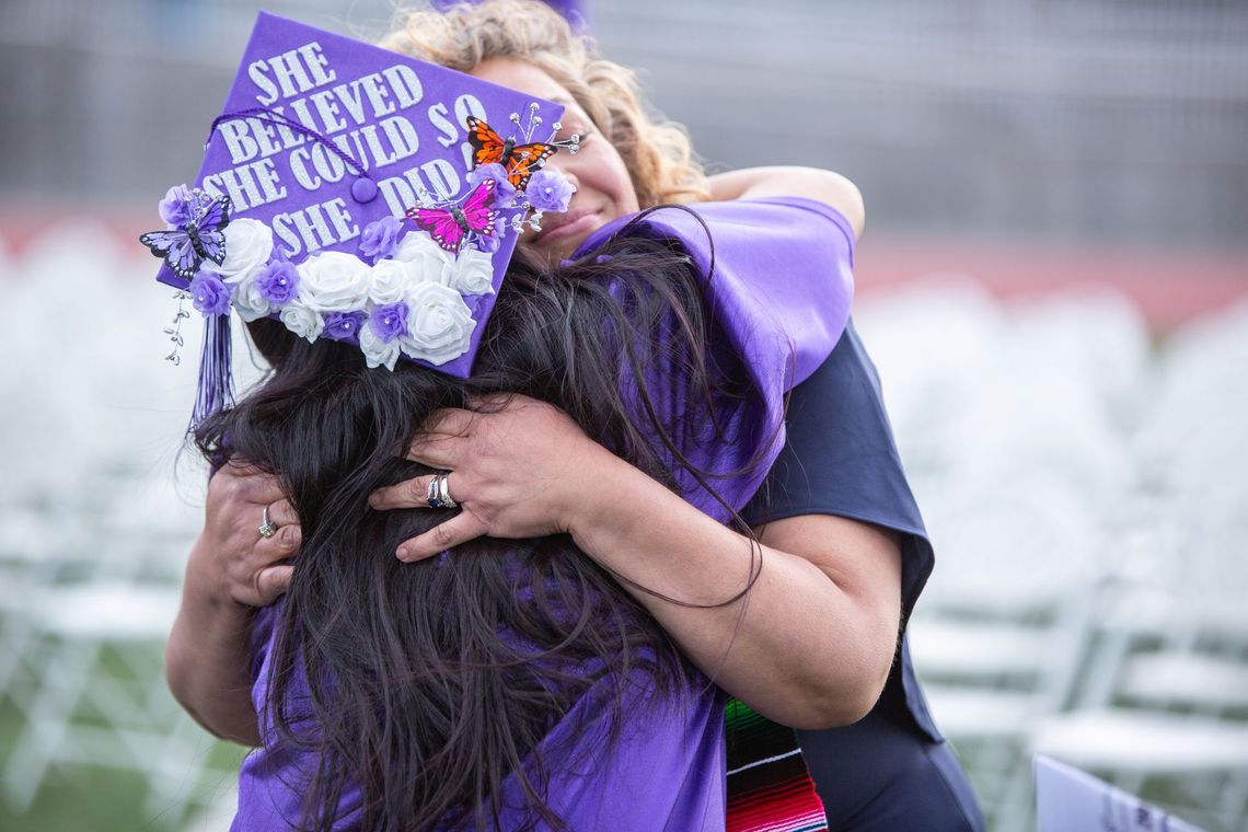 A woman is hugging a graduate wearing a purple graduation cap.