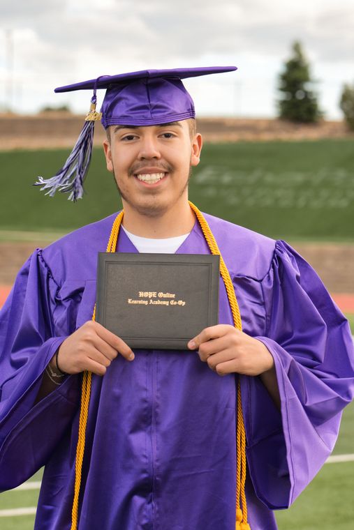 A man in a purple graduation cap and gown is holding a diploma.