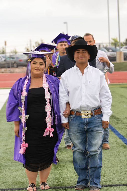 A woman in a purple cap and gown is walking with a man in a cowboy hat.