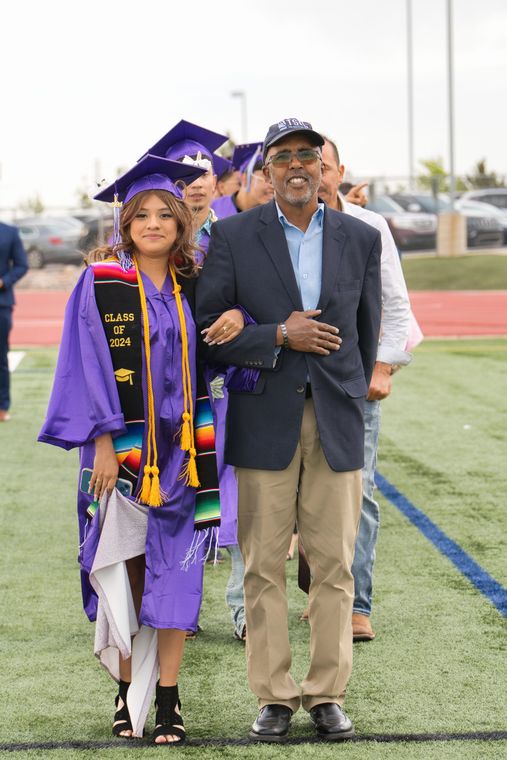 A man is walking a girl in a graduation cap and gown on a field.