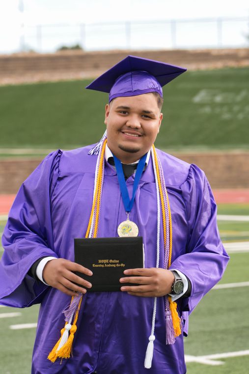 A man in a purple cap and gown is holding a diploma.