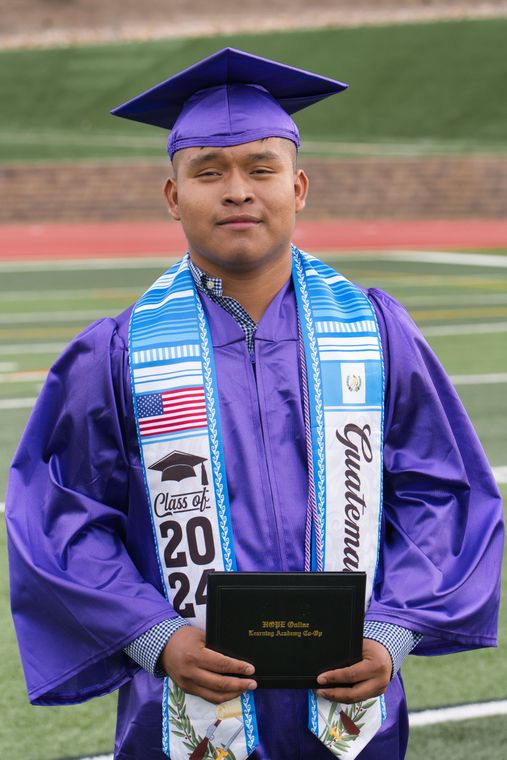 A man in a purple graduation cap and gown is holding a diploma.