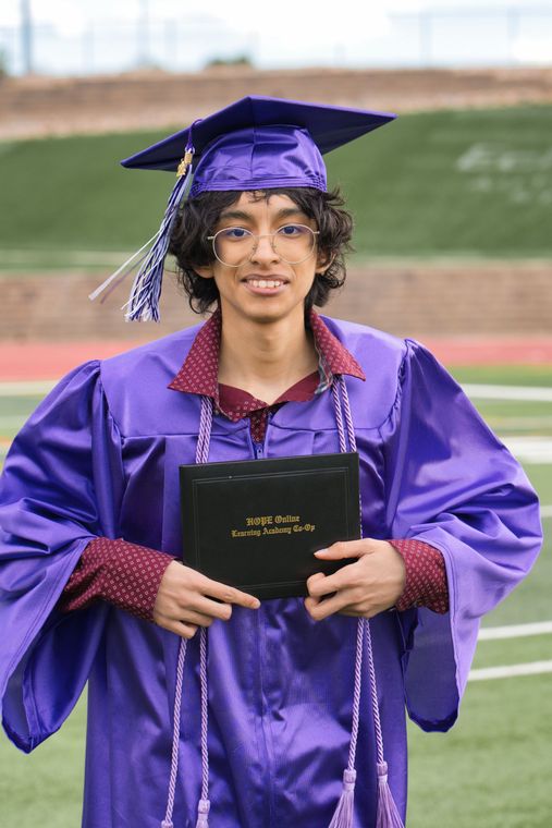 A young man in a purple graduation cap and gown is holding a diploma.