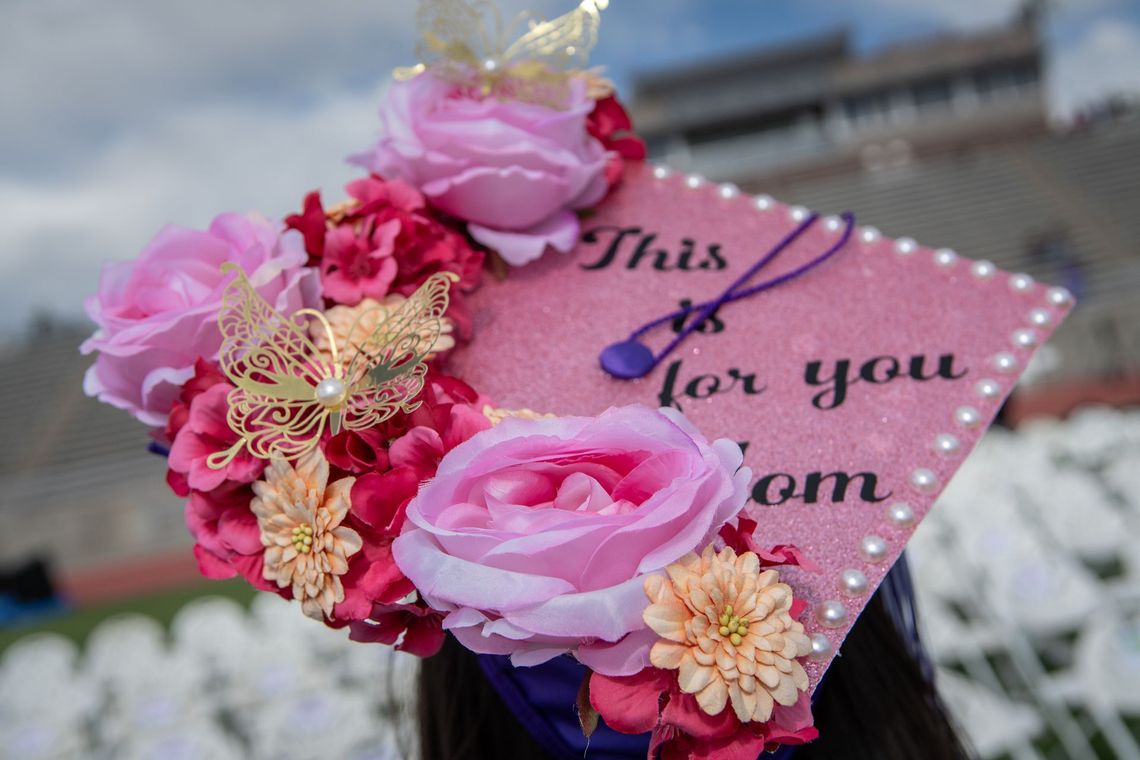 A woman is wearing a pink graduation cap decorated with pink flowers and butterflies.