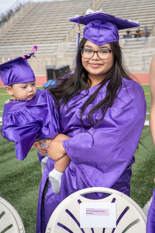 A woman in a purple graduation cap and gown is holding a baby.