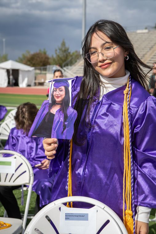 A woman in a purple cap and gown is holding a picture of herself.