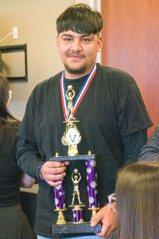 A young man is holding a trophy with a medal around his neck.