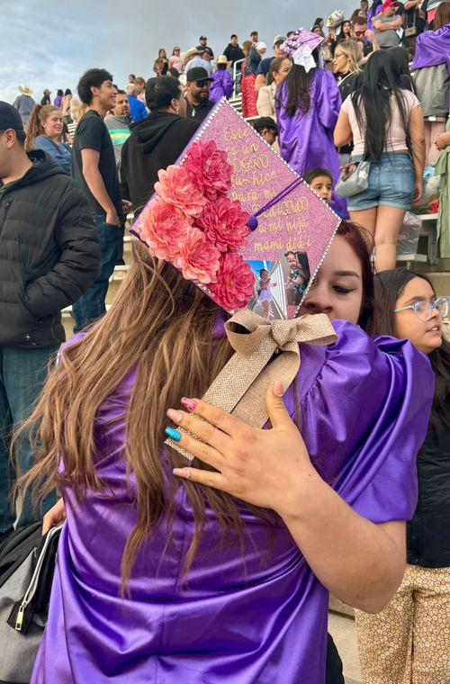 A woman in a purple dress is hugging another woman in a graduation cap.