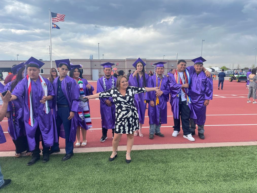 A woman is standing in front of a group of graduates.