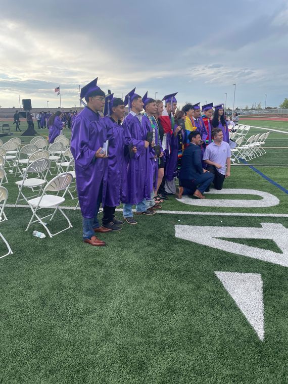 A group of graduates are standing in a line on a field.