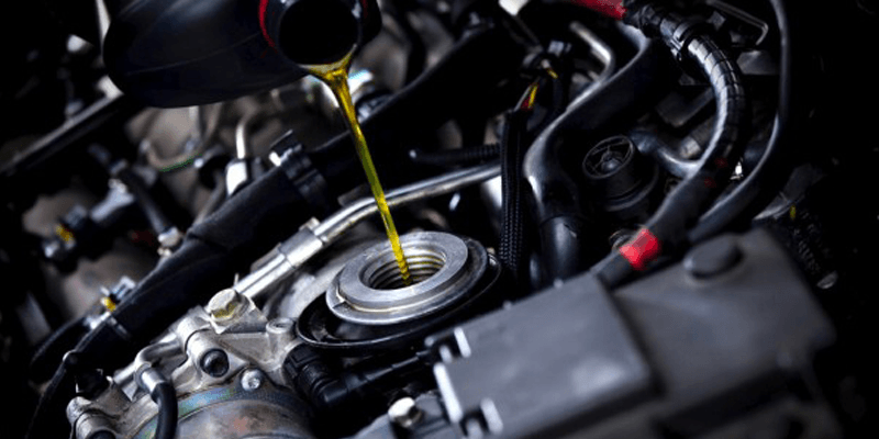 A close up of a person pouring oil into a car engine.