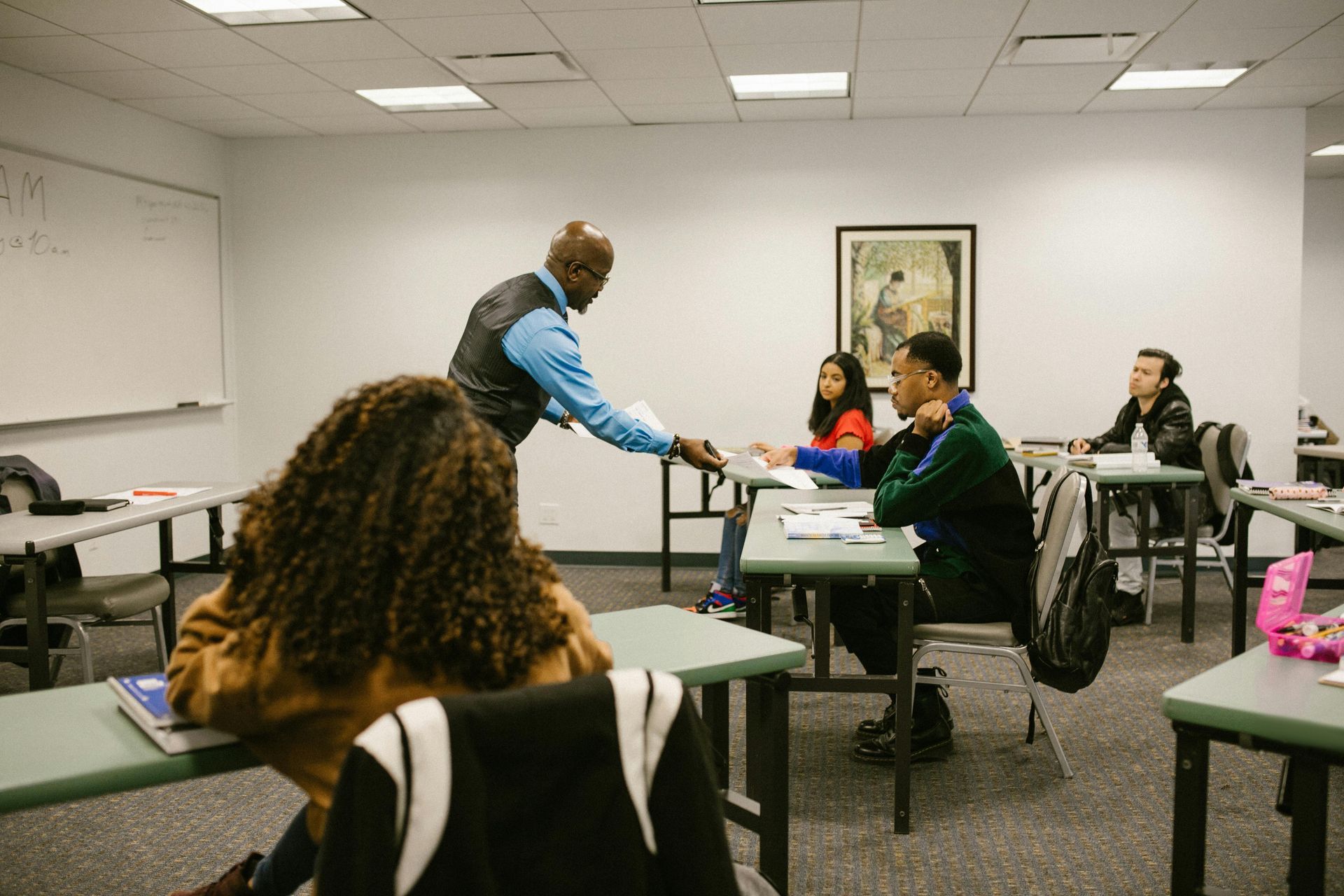 Teacher distributing papers to students in a classroom.