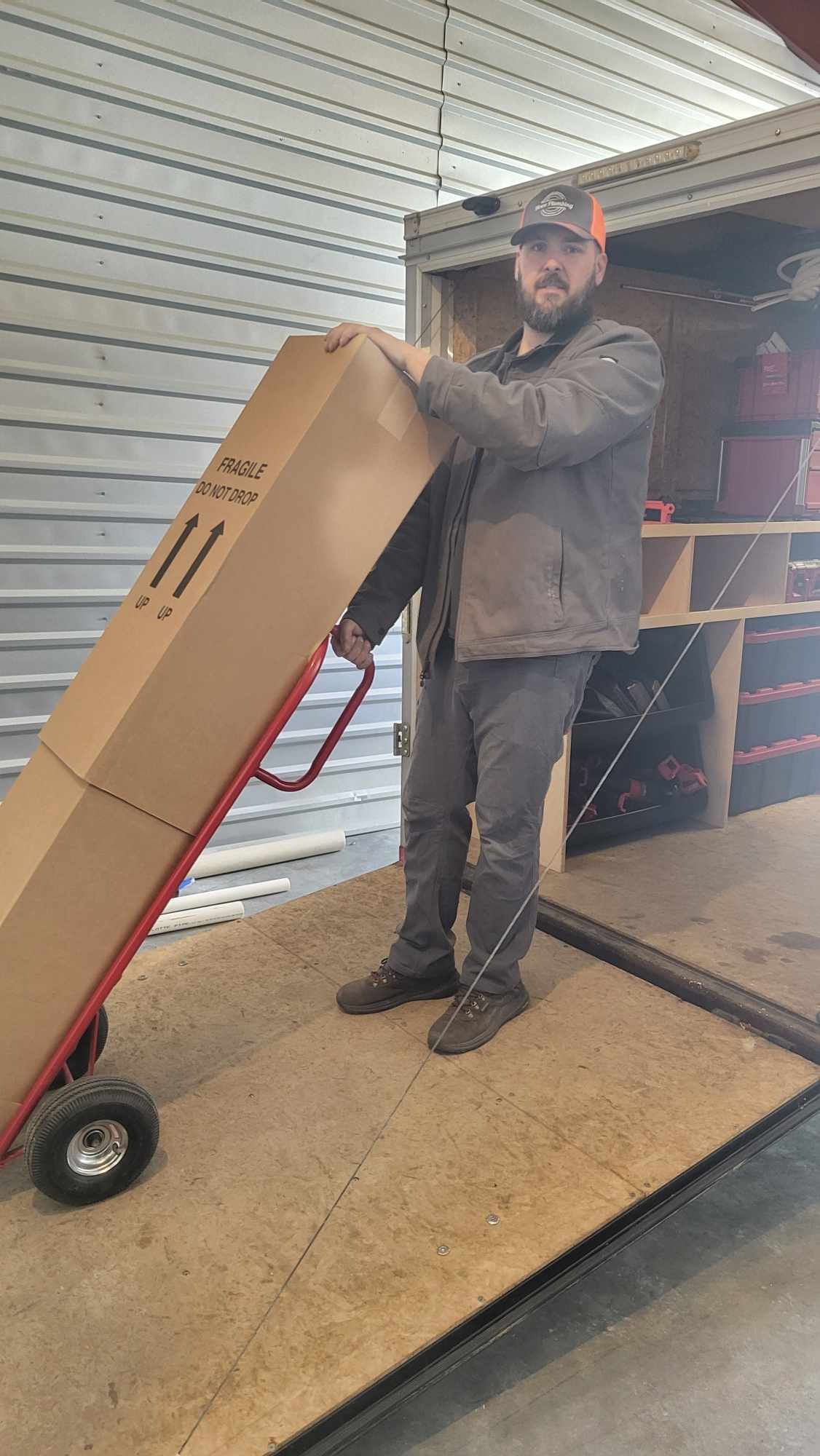 A man is pushing a cardboard box on a hand truck.