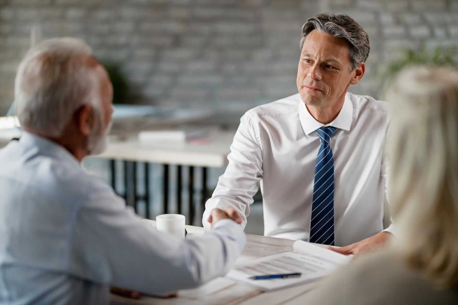 Two professionals shake hands over a document in an office setting.