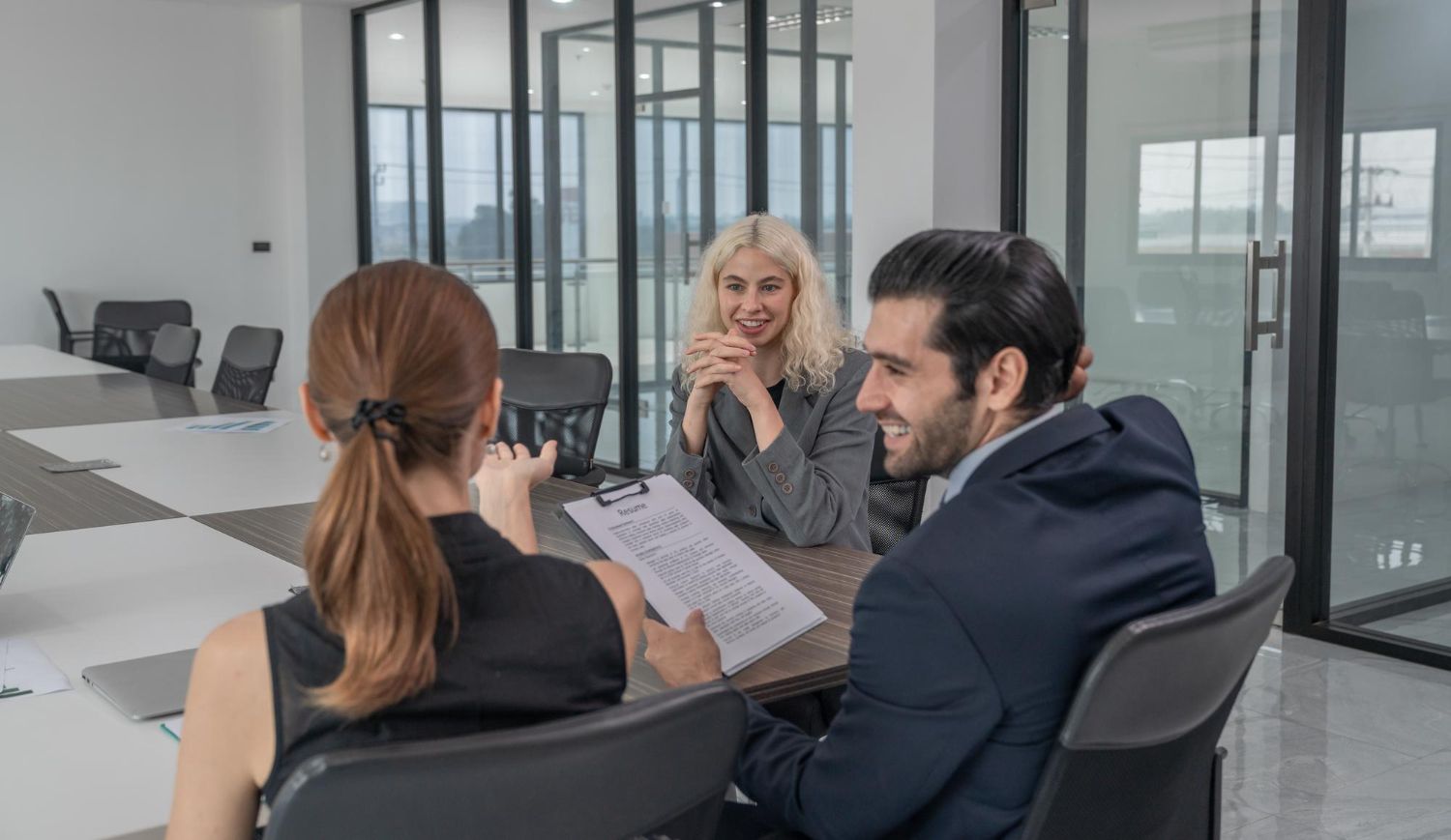 Three colleagues sit at a glass conference table in a modern office, engaged in a discussion over a document.