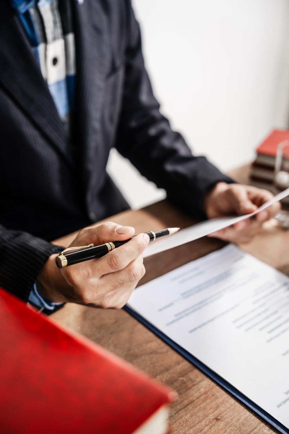A person in a suit and plaid shirt holding a black pen over a legal document on a wooden desk.