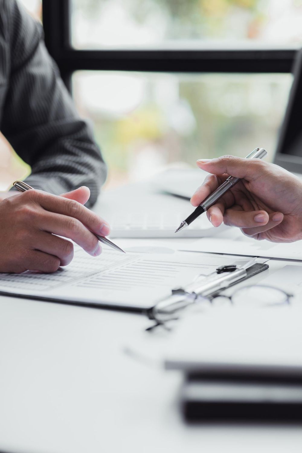 Two people reviewing documents on a desk, with one person pointing at the paper while holding a pen.