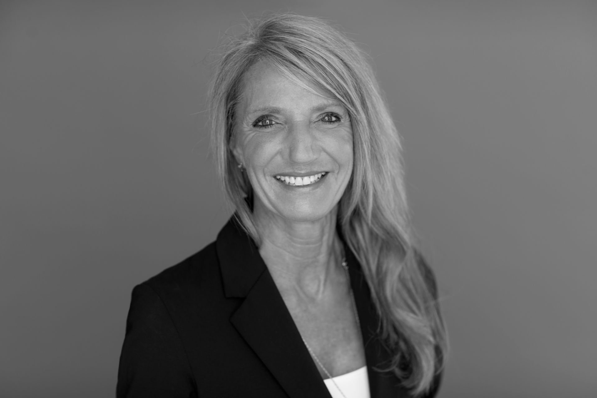 Et sort-hvidt foto af en kvinde i et jakkesæt, der smiler.