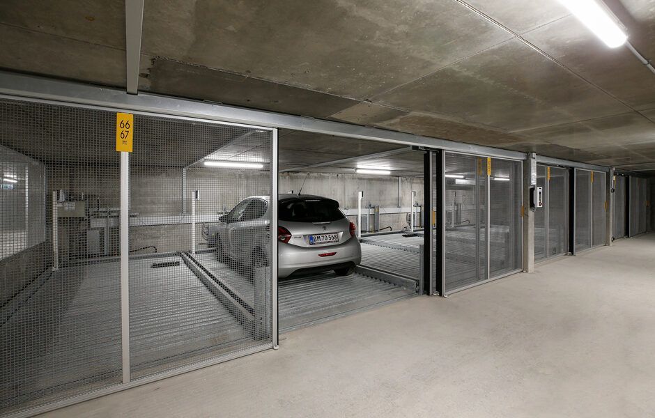 En bil er parkeret i et parkeringshus bag et hegn.