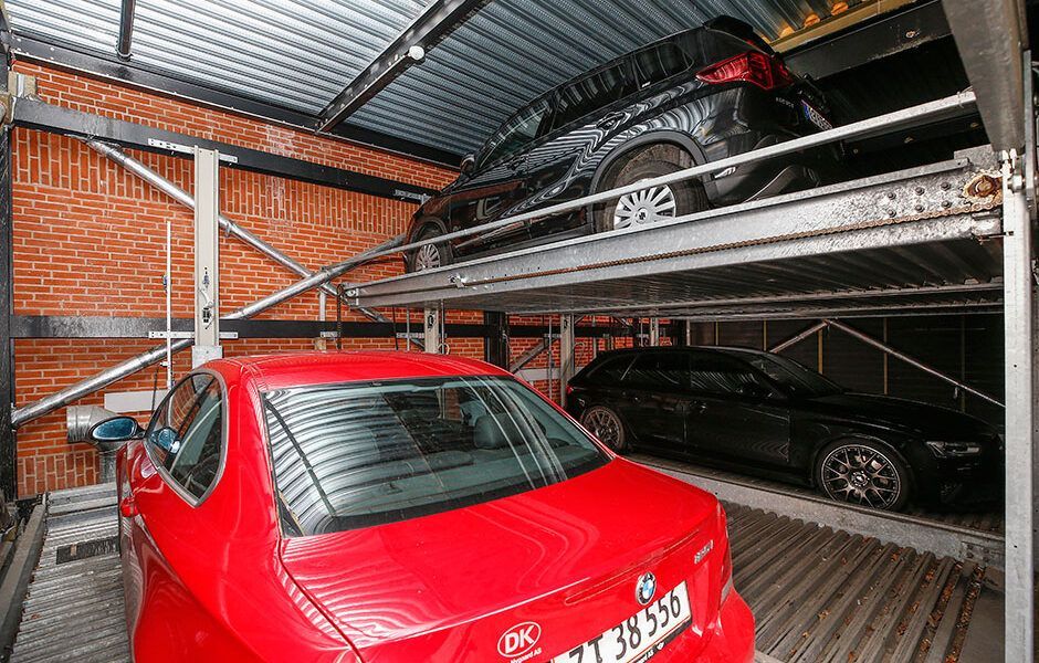 En rød bil er parkeret ved siden af ​​en sort bil i en parkeringskælder.