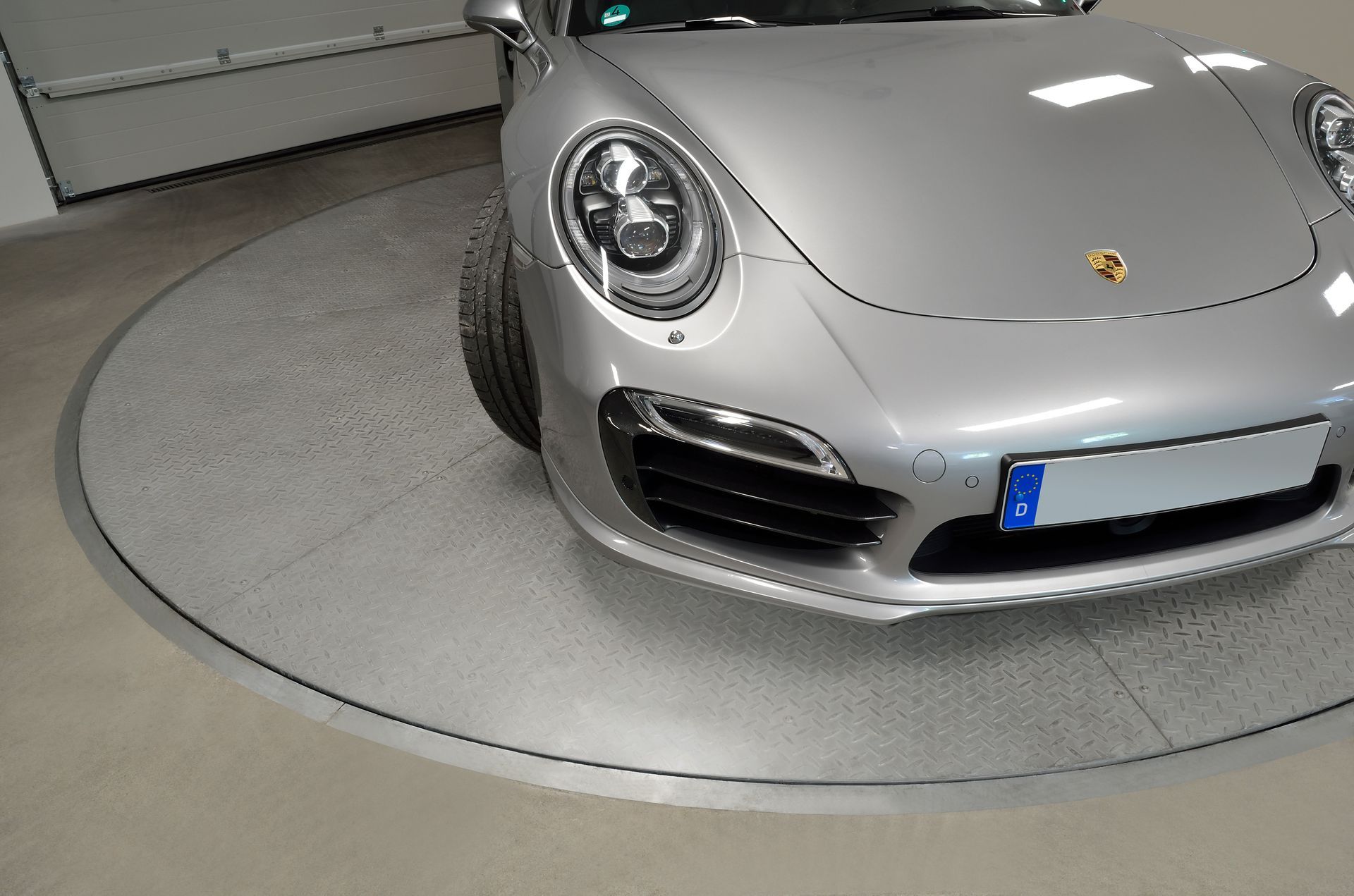 En sølvporsche er parkeret på en pladespiller i en garage