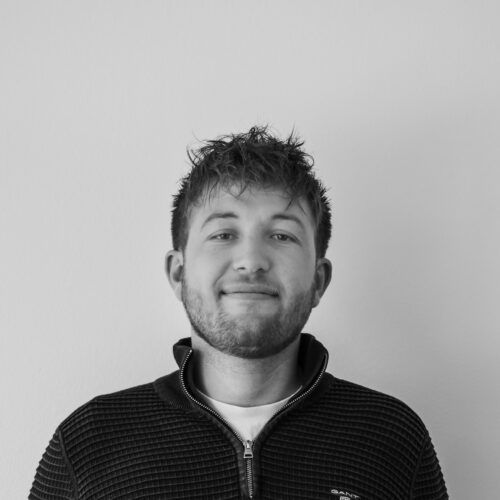 En mand med skæg er iført en sort sweater og smiler på et sort/hvidt foto.