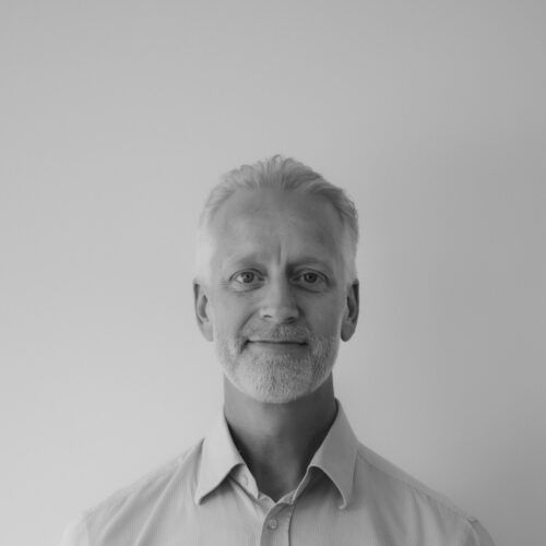 En mand med skæg smiler på et sort-hvidt foto.