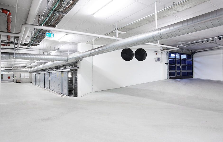 En stor tom underjordisk parkeringskælder med en masse rør, der kommer ud af loftet.