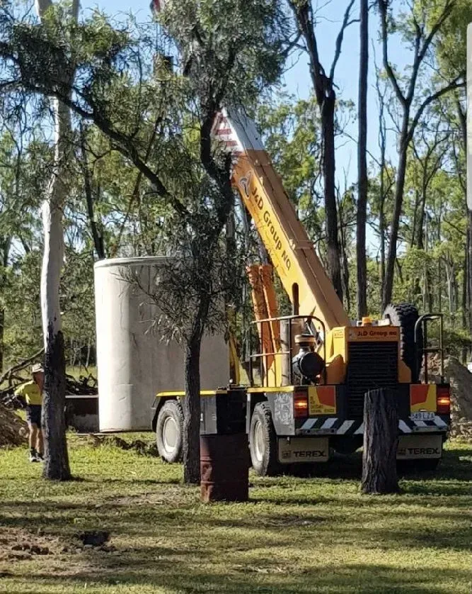 Crane Lifting a Large Cylindrical Water Tank in a Grassy Outdoor Area — MCA Plumbing & Drainage in Jensen, QLD