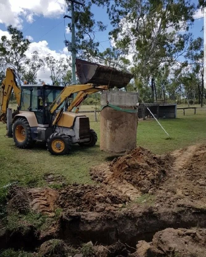Yellow Backhoe Moving a Concrete Structure in a Grassy Field  — MCA Plumbing & Drainage in Jensen, QLD