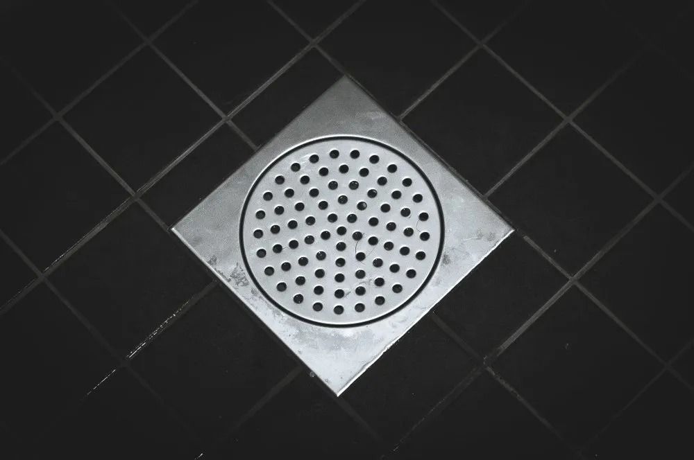 Square Metal Shower Drain in a Dark Tiled Floor — MCA Plumbing & Drainage in Jensen, QLD