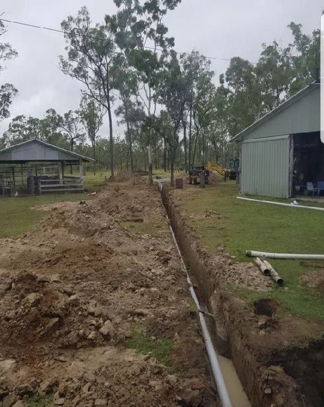 A Trench Dug in a Grassy Yard, With Pvc Pipe Installed — MCA Plumbing & Drainage in Jensen, QLD