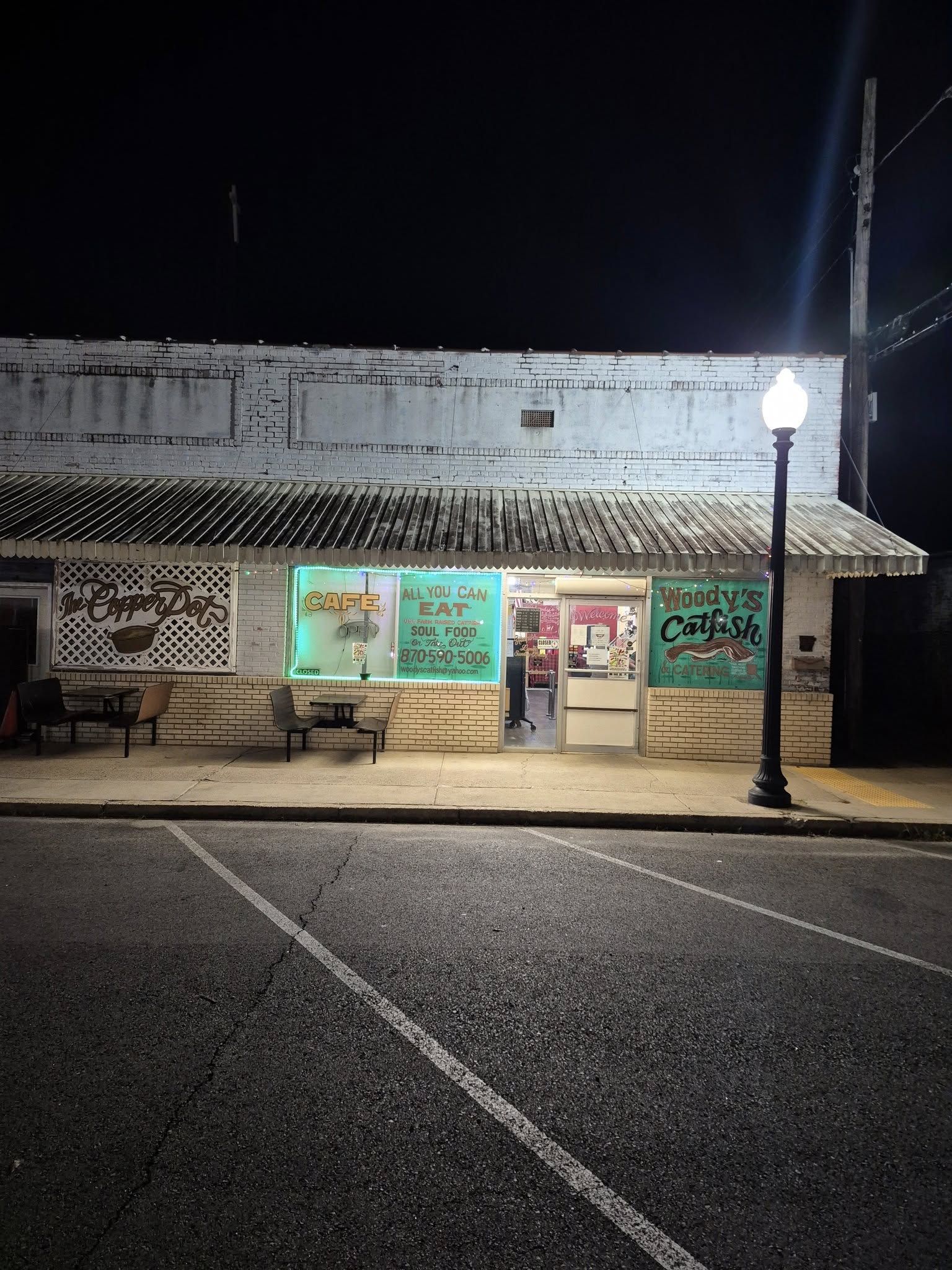 Nighttime view of a brightly lit shop with teal signs and a person inside. Streetlight illuminates the storefront.