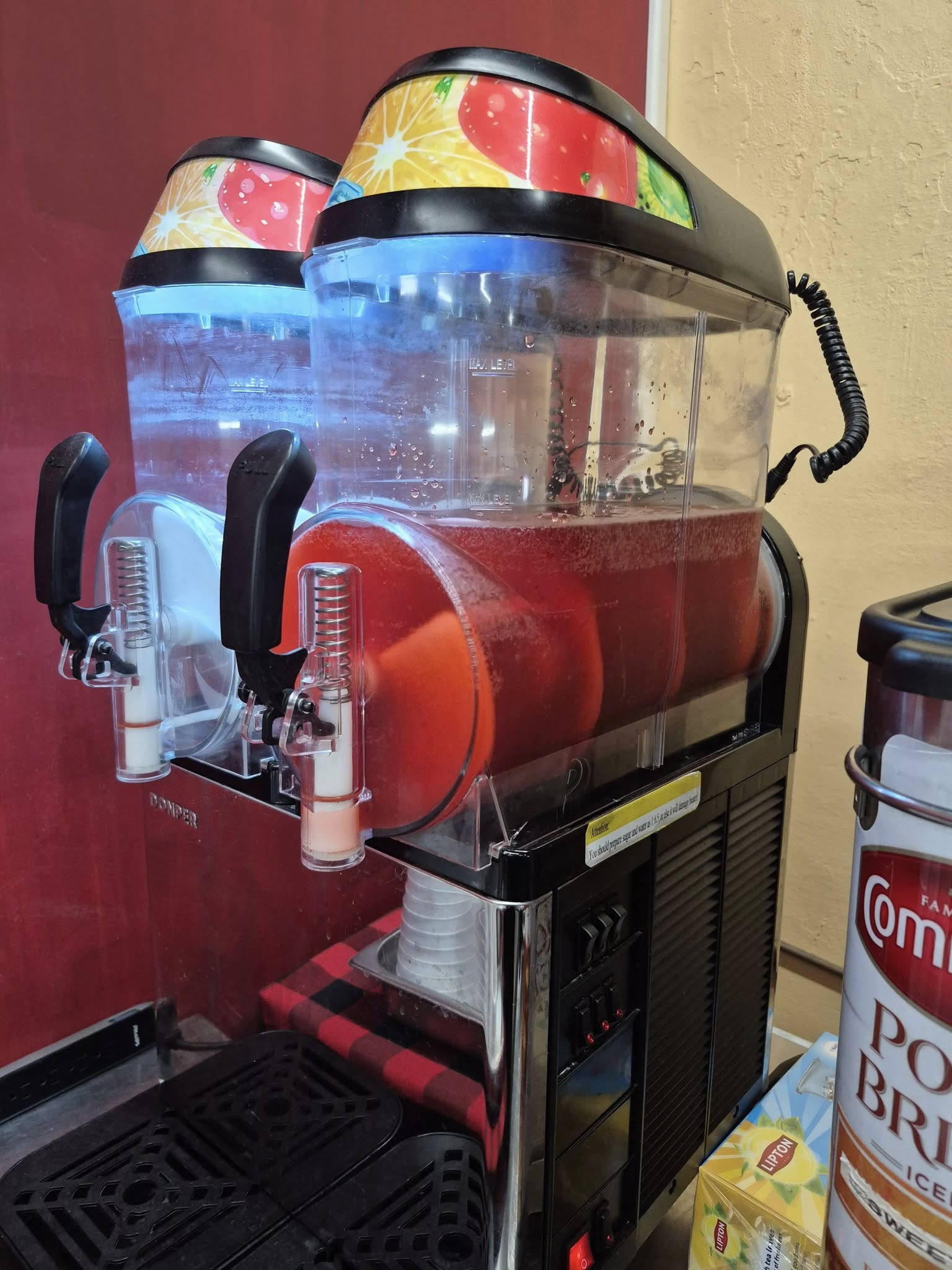 Dual-bowl slushy machine with red liquid, black accents, and fruit graphics.