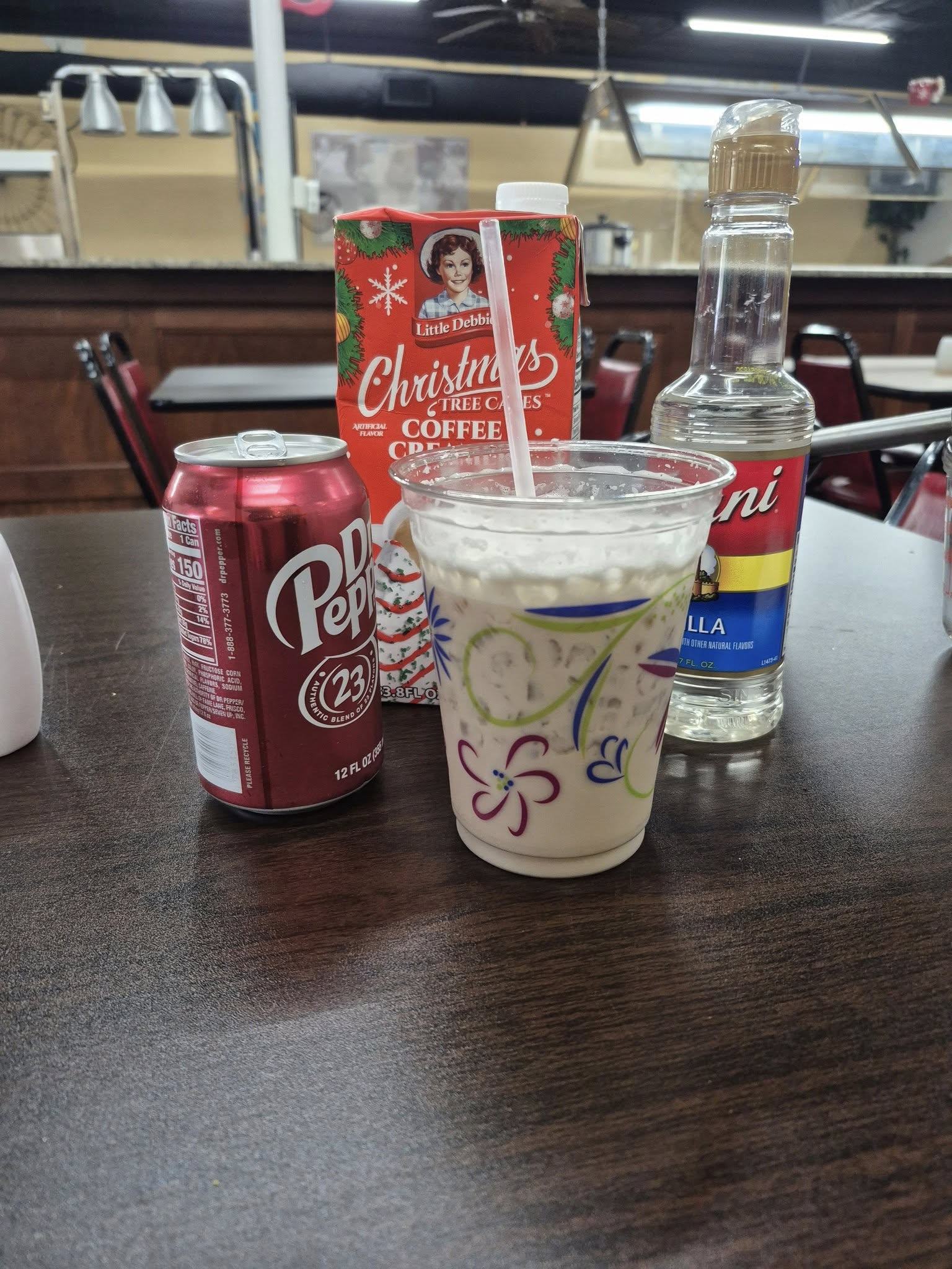 A Dr. Pepper can, carton, milkshake, and syrup bottle on a table in a diner.