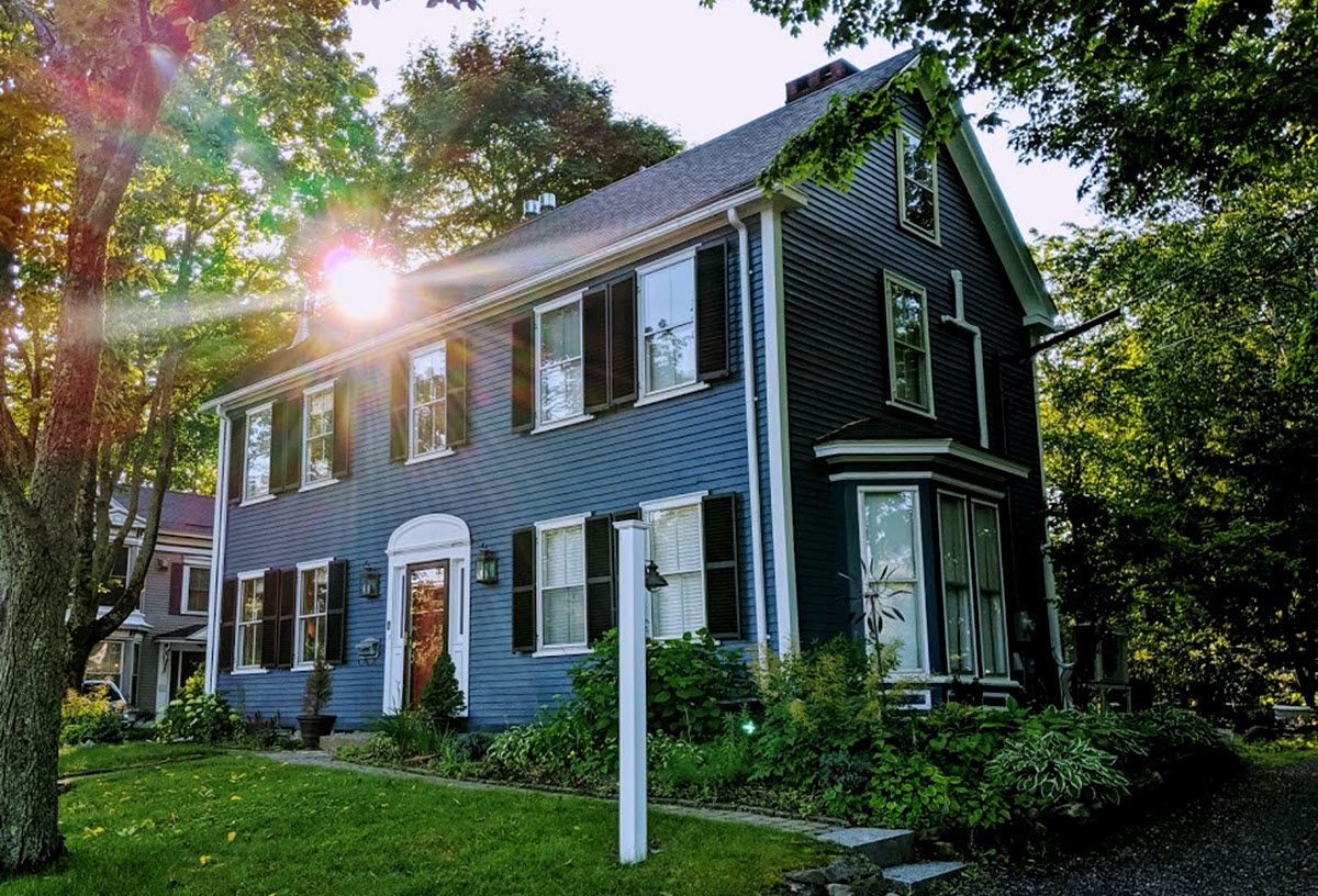 A large blue house with black shutters is surrounded by trees and grass.