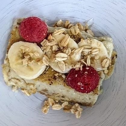 A close up of a plate of food with bananas , raspberries and granola.