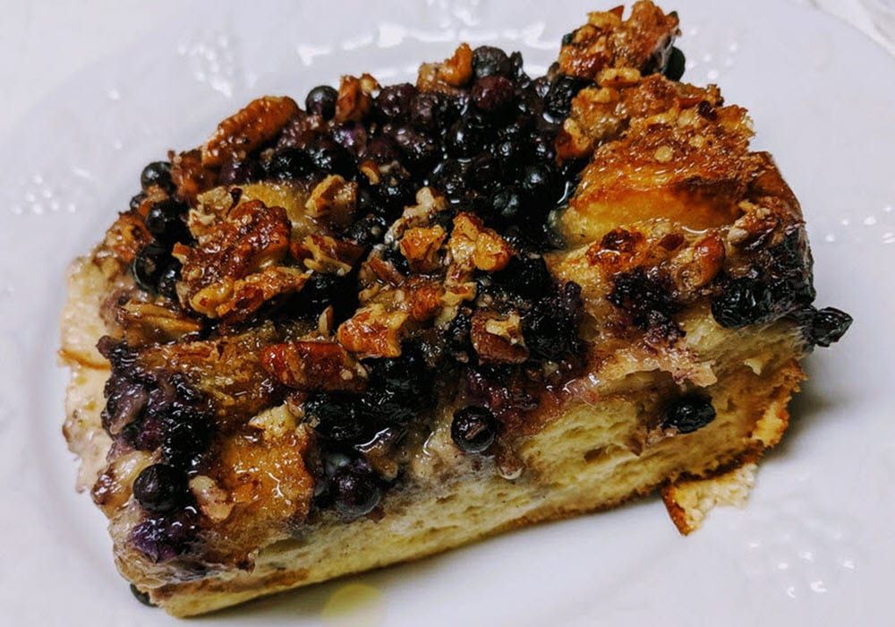 A piece of bread pudding with blueberries and pecans on a white plate
