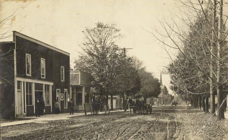 A black and white photo of a horse drawn carriage on a dirt road