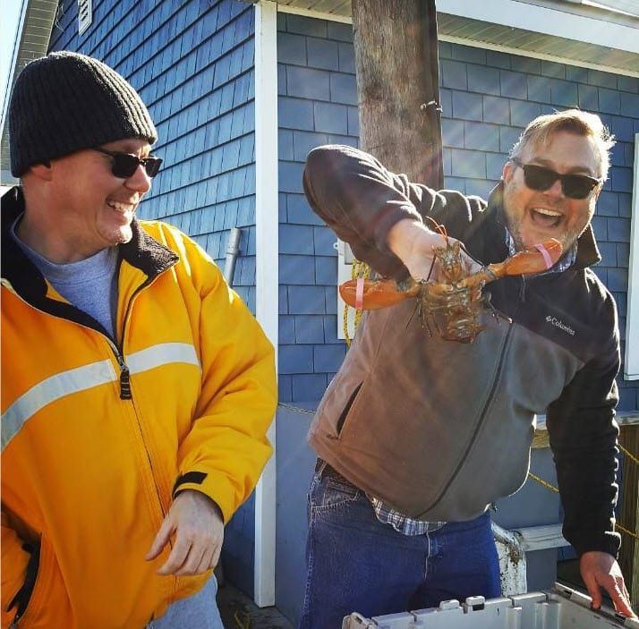 A man in a yellow jacket is holding a lobster