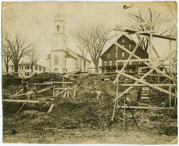 A black and white photo of a construction site with a church in the background