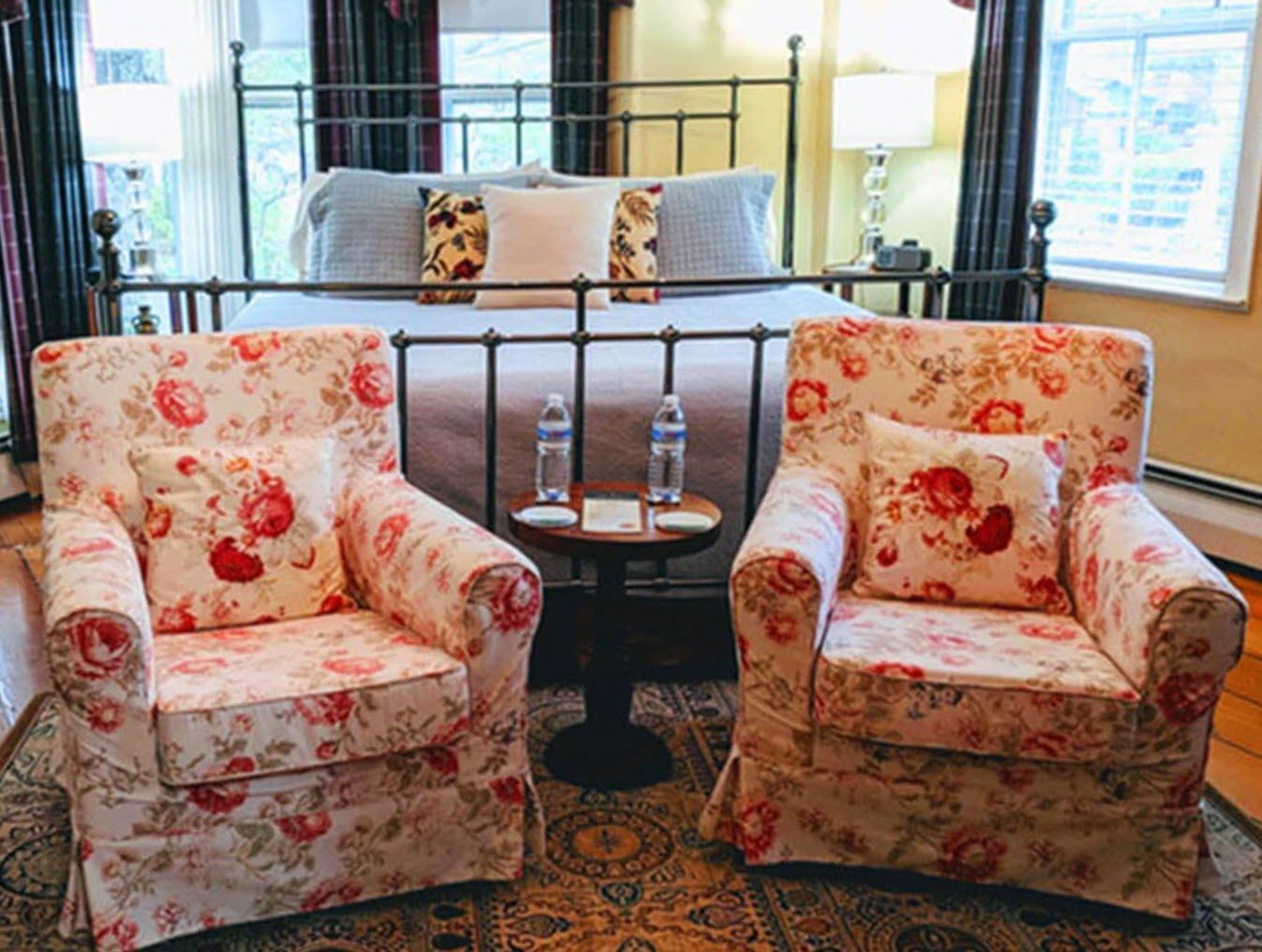 A bedroom with two chairs and a table in front of a bed.