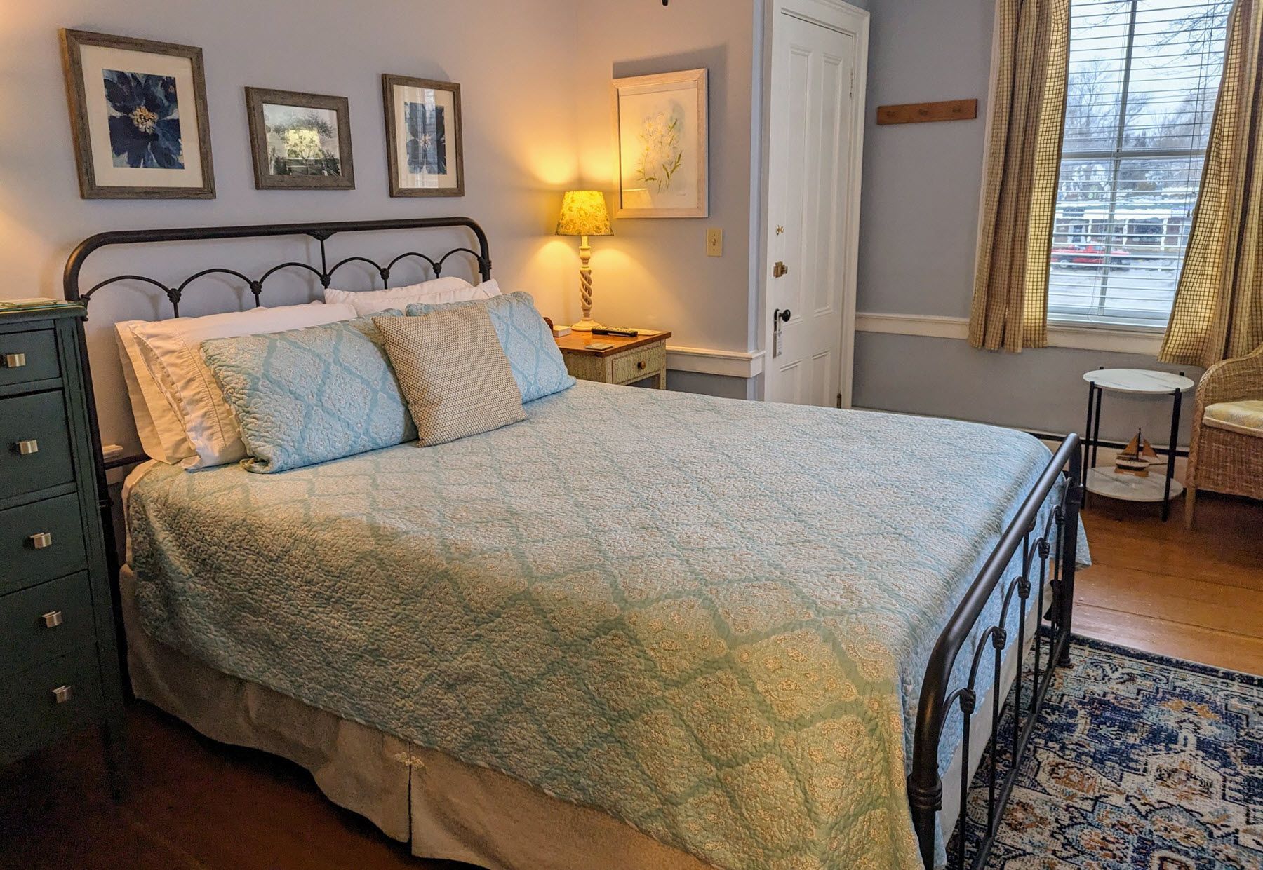 A bedroom with a bed , dresser , lamp and window.