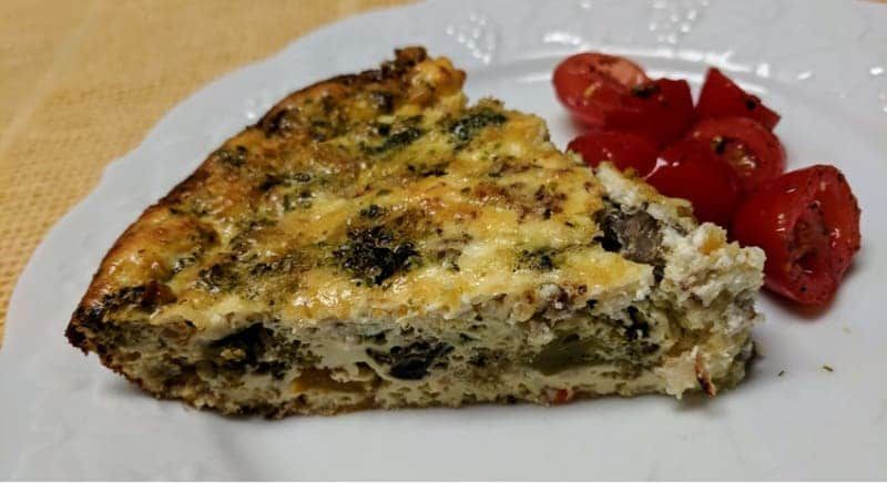 A white plate topped with a slice of quiche and tomatoes