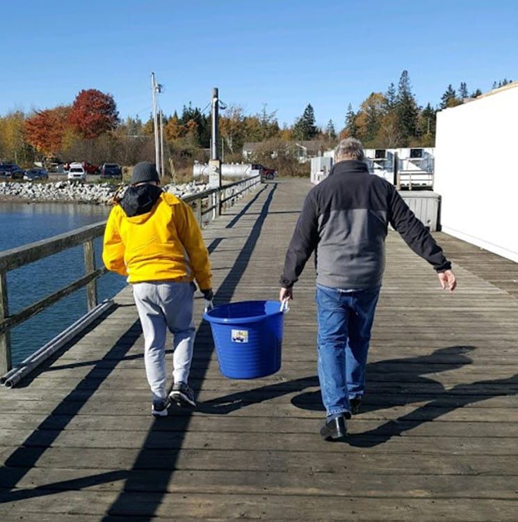 Two men are walking on a dock carrying a blue bucket